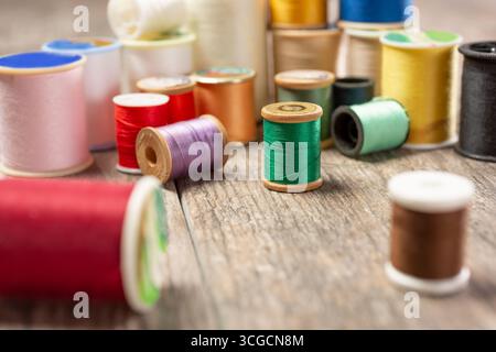 A closeup view of a variety of of thread spools in different colors, on a wooden surface. Stock Photo