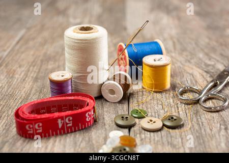 A closeup view of objects contained in a common sewing kit, featuring thread spools, tape measure, scissors, buttons and a needle. Stock Photo