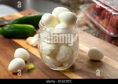 A view of a mason jar filled with hard boiled quail eggs, on a cutting board, in a kitchen setting. Stock Photo