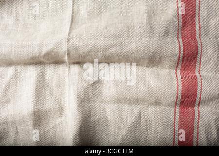 A top down view of a casually wrinkled rustic beige kitchen cloth towel with with a red stripe, as a background image. Stock Photo