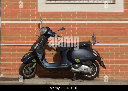 Metallic blue Vespa motorcycle parked on the sidewalk in front of a brick wall and window Stock Photo
