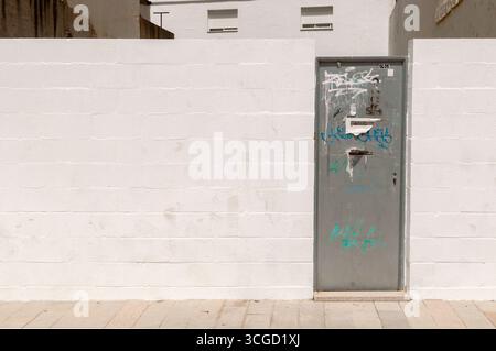 A white wall or wall ideal for graffiti or murals, with a metal gate. A wall for a construction project, on an empty lot, with a plain white wall. Stock Photo