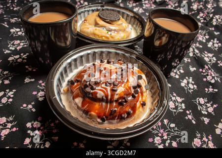 A breakfast or dessert setting with two different cinnamon buns one with chocolate and one with a cookie served with two black mugs of coffee on a flo Stock Photo