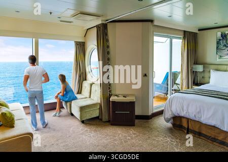 A couple enjoys the sea views from a picture window in their luxury balcony suite on a cruise ship at sea. Stock Photo