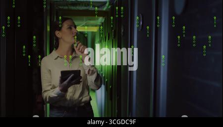 Analyzing IT engineer in jeans holding tablet in server corridor, with racks cables binary overlay Stock Photo