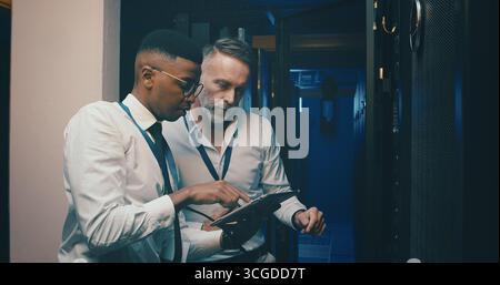 Engineer, men and planning with tablet, server room and teamwork for software upgrade or discussion. Data center, people and review of information Stock Photo