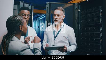 Server room, training and people on tablet for cybersecurity, diagnostics test or maintenance. IT team, meeting and workers with boss on digital tech Stock Photo