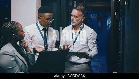 Talking, network and people with laptop in server room for cybersecurity, diagnostics and IT support. Team, meeting and workers on tech, tablet and Stock Photo