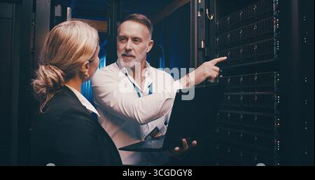 Laptop, pointing and team of engineers in server room for technical support, database or cybersecurity. Computer, teamwork and people with system Stock Photo