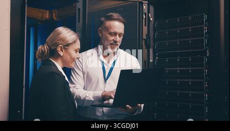 Laptop, discussion and team of engineers in server room for technical support, database or cybersecurity. Computer, collaboration and people with Stock Photo