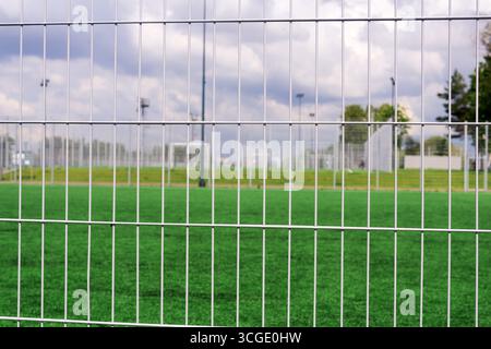 Sports grounds and soccer field behind a metal fence with green grass and blue sky Stock Photo