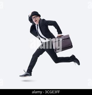 A businessman wearing a bowler hat and holding a briefcase runs away, scared and frightened, isolated on a white background. Stock Photo