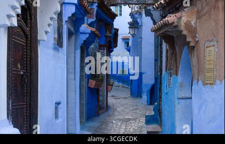 Narrow alley in the medina of Chefchaouen, Morocco—“the Blue City”—with cobalt-painted walls and doors, hanging street lamps. Stock Photo