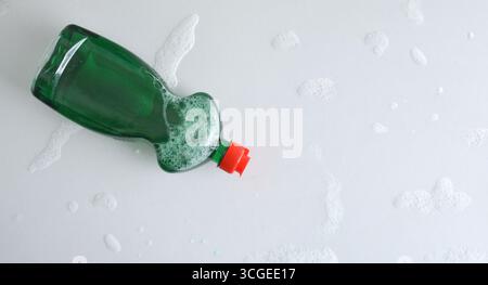 Background with a plastic dishwasher bottle with green product and red cap on a white kitchen counter with traces of water and foam. Top view. Stock Photo