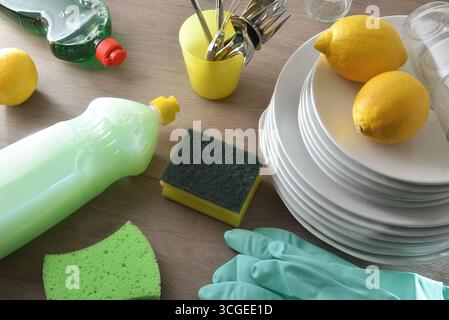 Ecological and chemical dishwashing product on a wooden kitchen bench with utensils such as scouring pads, gloves and a stack of plates with lemons, g Stock Photo