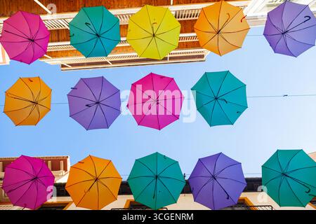Multi-colored umbrellas hang on the street along the houses against the sky. Stock Photo