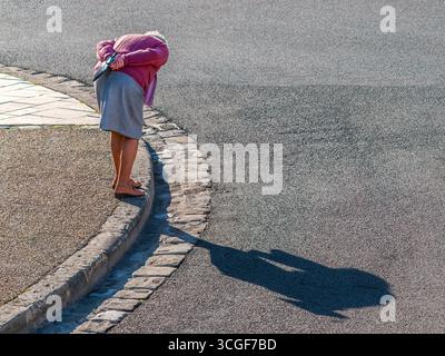 Overhead view of elderly woman bending down at side of road casting a long shadow - Preuilly-sur-Claise, Indre-et-Loire (37), France. Stock Photo