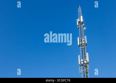 White antennas on cell tower close-up. Mobile data transmission tower with antennas against a blue clear sky, concept of telecommunications equipment, Stock Photo