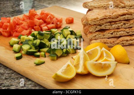 Cutting Board with Chopped Cucumber, Tomatoes, Lemon, and Pita Bread Stock Photo