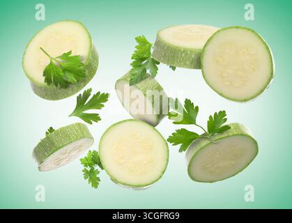 Fresh zucchini slices and parsley falling on green gradient background Stock Photo