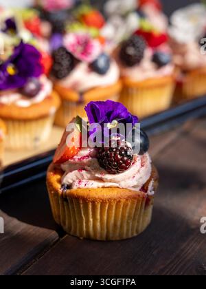 Hero summer berry cupcake by Peggy Porschen with berry meringue frosting, topped with strawberry, blueberry, blackberry, and edible flower. Stock Photo