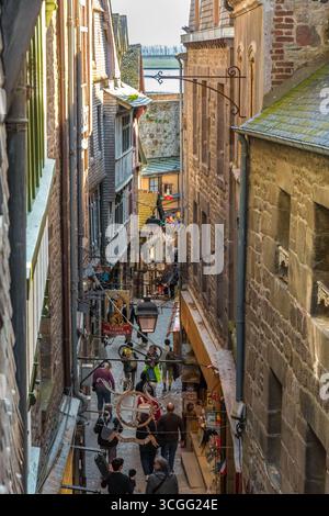 Lovely view overlooking Mont-Saint‑Michel’s narrow, winding main street Grande Rue towards the lower section. Old‑style hanging signs of shops,... Stock Photo