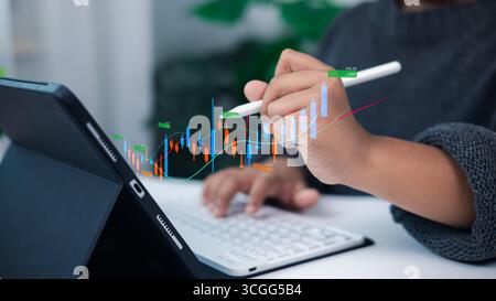 Person analyzing financial growth and market data on digital tablet with stylus, holographic stock chart and candlestick graph, concept of modern inve Stock Photo