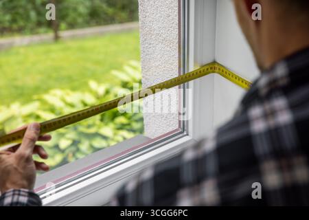man measuring white plastic window frame for replace Stock Photo