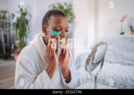 Young woman applying hydrogel eye patches and looking in the mirror Stock Photo