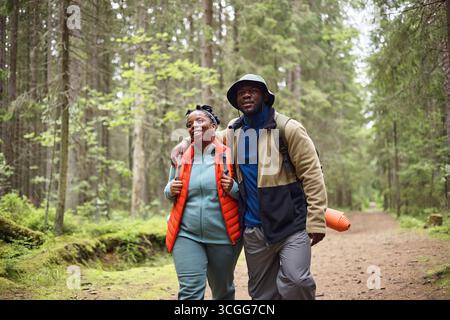 Young Black Couple Hiking Together in Forest and Smiling at Camera Stock Photo