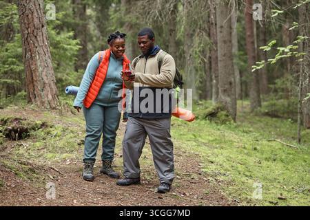 Young Black Couple Hiking in Forest Using Smartphone for Navigation Stock Photo