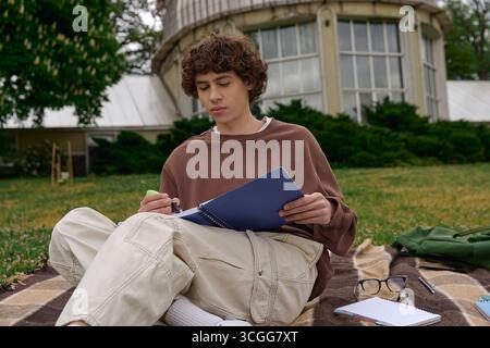 A young handsome student relaxes outdoors, focused on his studies while sitting on a blanket. Stock Photo