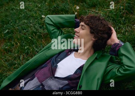 A young handsome student lies on the grass, embracing the calmness of nature. Stock Photo