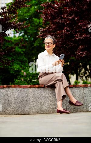 Professional businesswoman outdoors using smartphone, enjoying spring day in the city with a modern urban setting Stock Photo