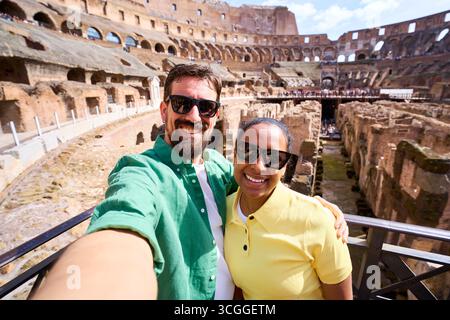 Smiling couple taking a selfie with colosseum in background during their roman vacation Stock Photo