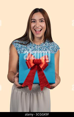 Excited young woman holding a blue gift box with a red bow, surprised by a present Stock Photo