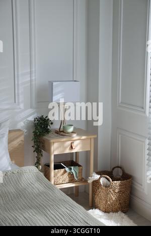 Bedside table with lamp and other decor near bed indoors Stock Photo