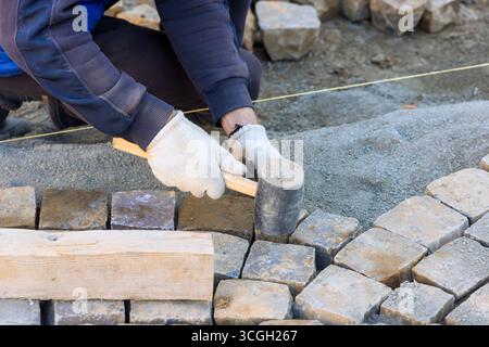 Worker installs stone pavers on prepared surface, carefully aligning each piece with precision. Stock Photo
