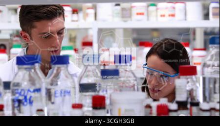 Two scientists in lab coats leaning over lab bench analyzing samples with reagent bottles, overlays Stock Photo