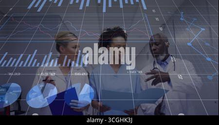 Medical team in lab coats reviewing documents in hospital corridor, with clipboard data charts Stock Photo