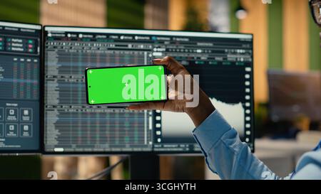 Close up of portfolio manager using mockup smartphone to watch trading educational content. Hedge fund professional in office learns new trading strategies from video lesson on green screen phone Stock Photo