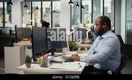 Portfolio manager in prop firm office analyzes stock market trends to enhance investment returns. African american man tracks performance metrics to identify investment opportunities Stock Photo