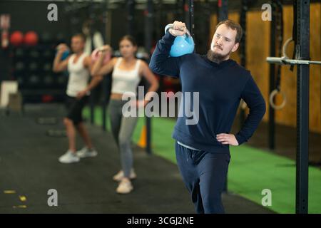 Bearded man doing kettlebell overhead shoulder press in gym Stock Photo