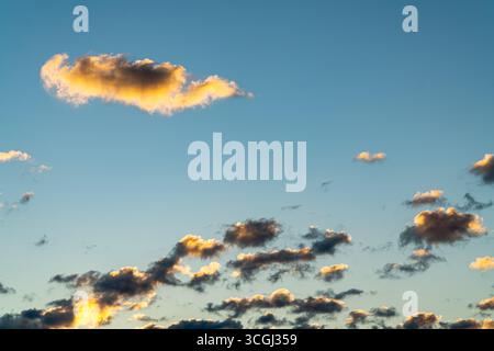 Scattered small clouds and one larger cloud illuminated by warm sunset light in a blue sky. Stock Photo