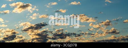 Small scattered clouds drift across a clear blue sky, illuminated by the golden tones of the setting sun. Stock Photo