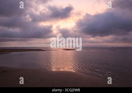 A bright sunray passing through pink cloud layers and lighting the ocean, with mirrored clouds on the beach’s edge Stock Photo
