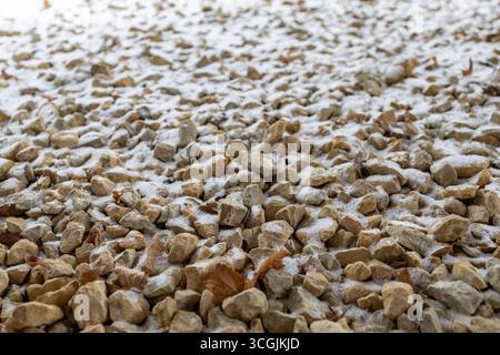 Close up abstract texture background of a fine layer of fresh white snow on crushed tan color landscaping rocks Stock Photo
