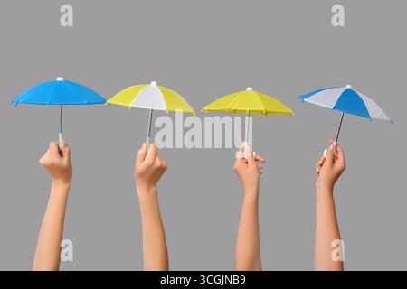 Female hands with different mini umbrellas on grey background Stock Photo
