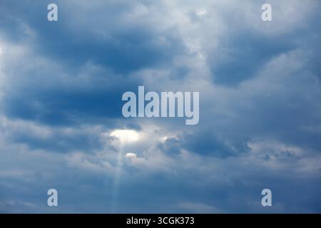 Sunbeams break through a dense cloud cover, casting a dramatic light on the sky. Atmospheric view of a sky filled with dark, textured clouds Stock Photo