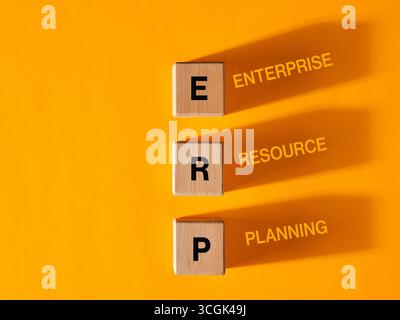 Wooden cubes with letters composing the acronym ERP, enterprise resource planning, casting their shadow on an orange background Stock Photo